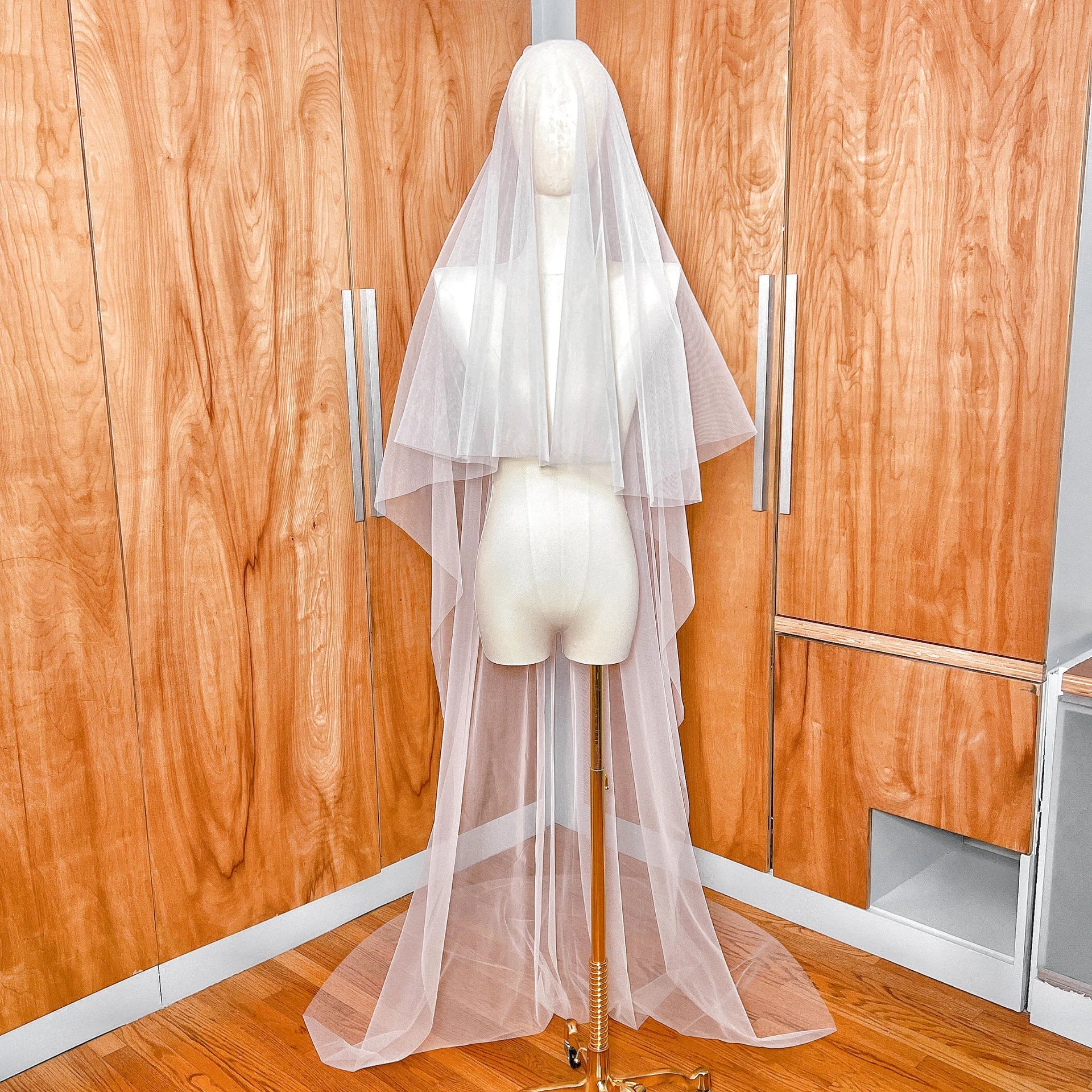 Front view of a simple two-tier chapel length wedding veil with a sheer blusher and minimalist raw edge draping elegantly over a bridal mannequin.