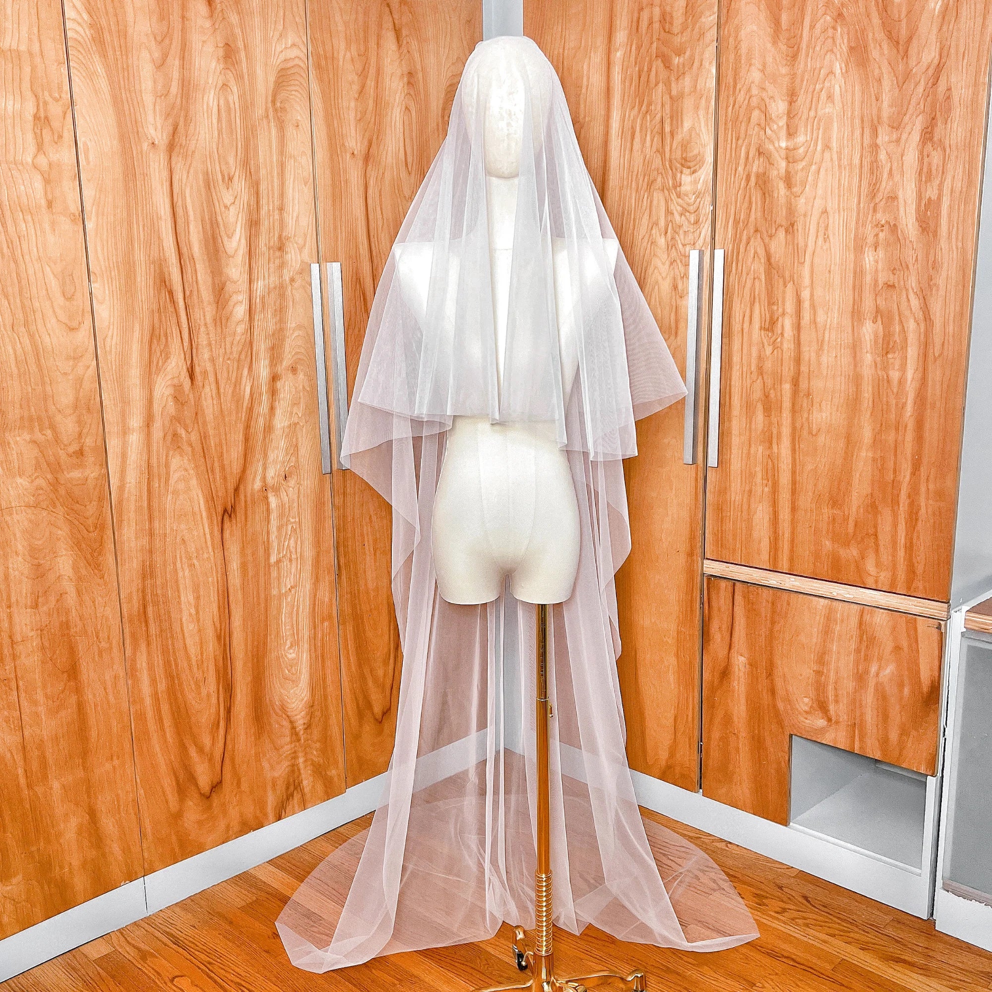 Front view of a simple two-tier chapel length wedding veil with a sheer blusher and minimalist raw edge draping elegantly over a bridal mannequin.