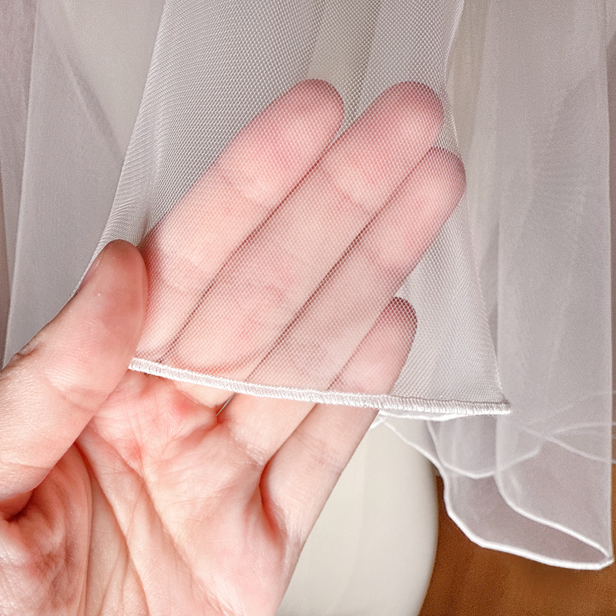 Close-up of the delicate pencil edge stitching on a simple two tier elbow length wedding veil.
