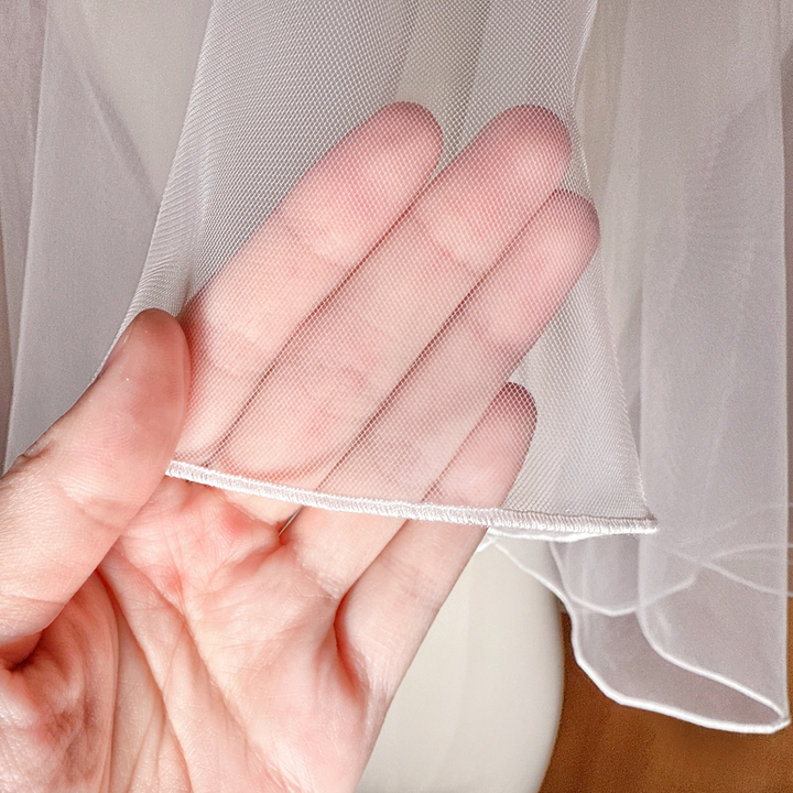 Close-up of the delicate pencil edge stitching on a simple two tier elbow length wedding veil.