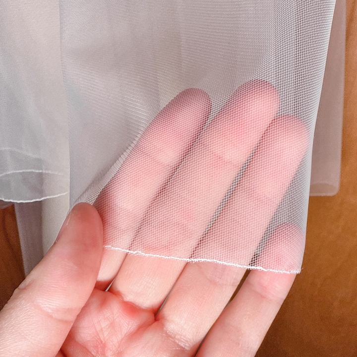 Close-up shot of the sheer tulle fabric and stitched pencil edge on a simple two tier wedding veil.