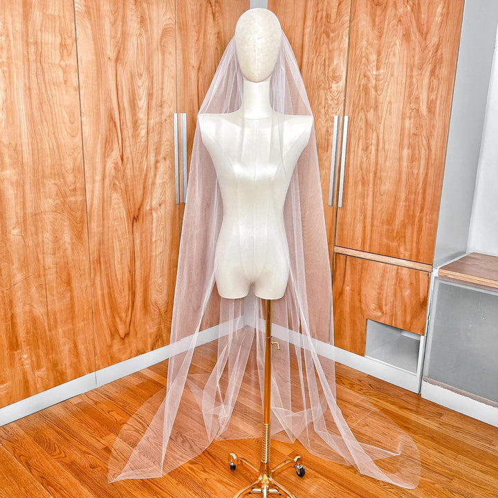 Full length view of a single tier chapel length tulle veil with a soft raw edge draped elegantly onto the floor.