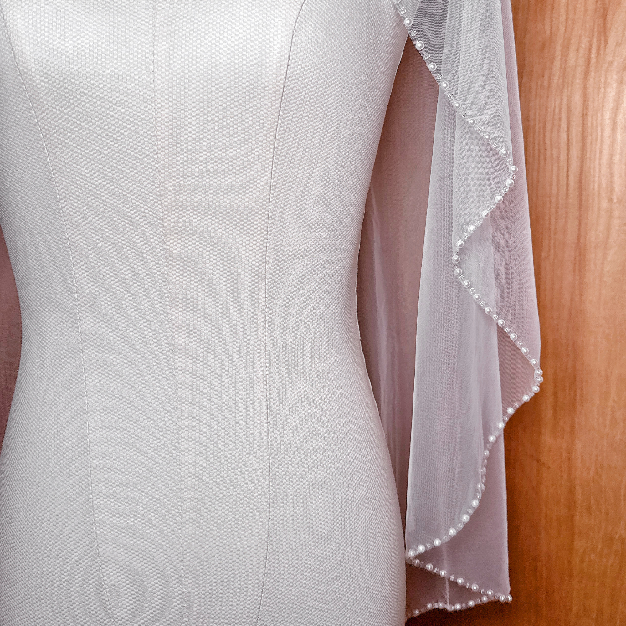 Single-tier ivory fingertip wedding veil decorated with a continuous line of lustrous pearls.