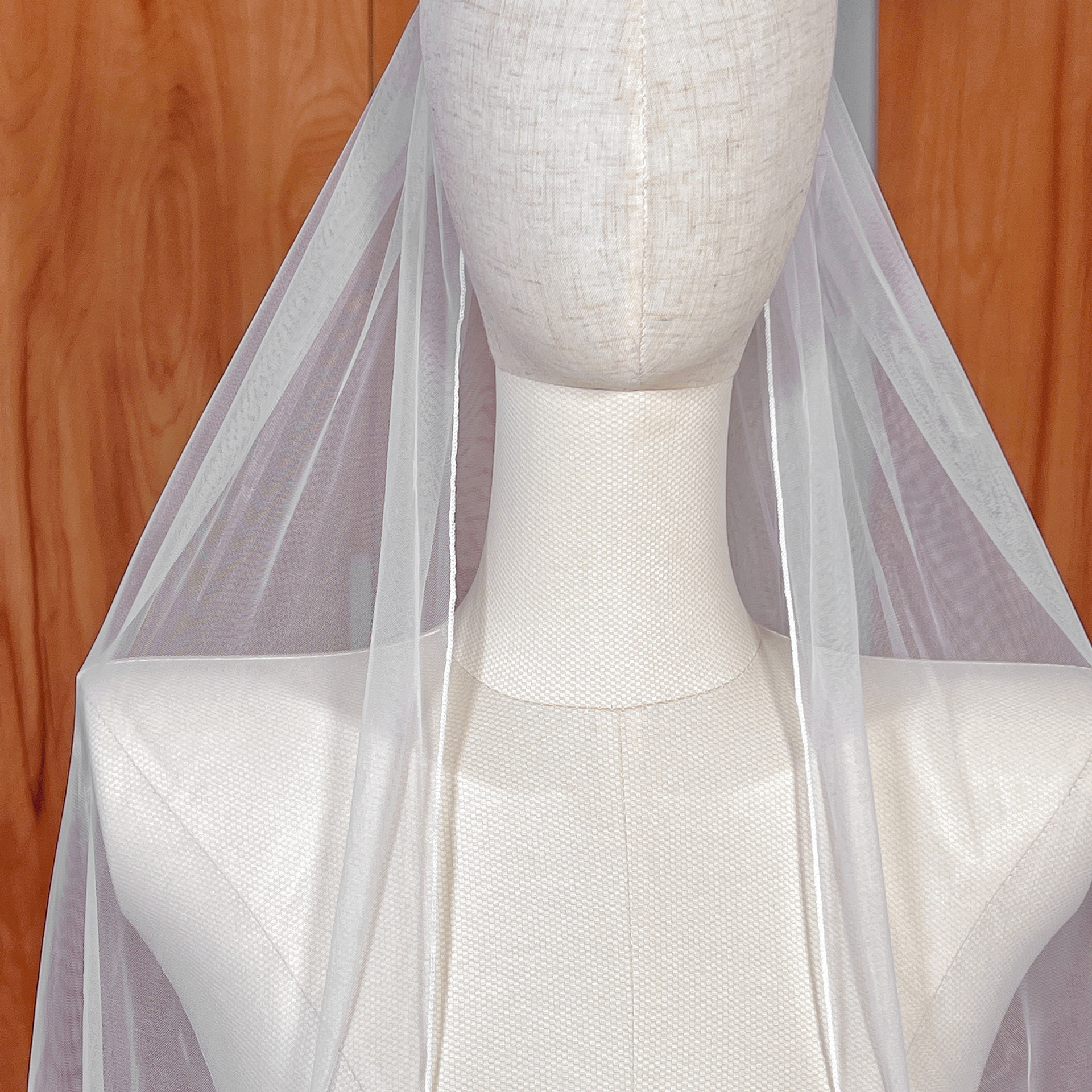 Sheer bridal tulle of a fingertip single tier pencil edge wedding veil on a mannequin.