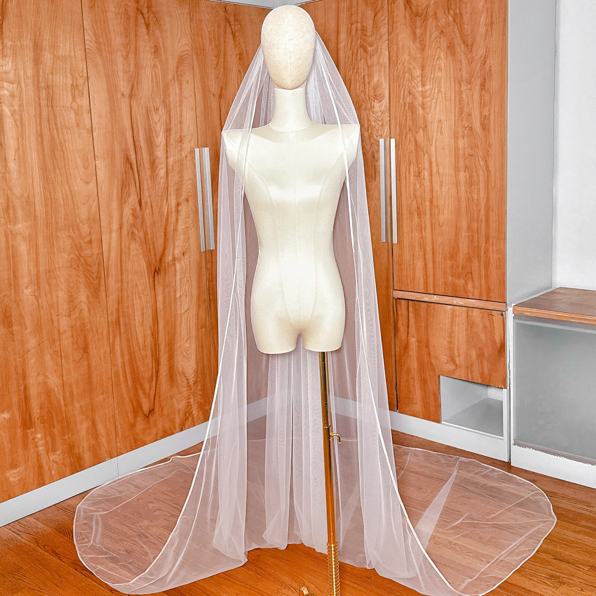 Cathedral length single tier ribbon edge wedding veil cascading down a display torso.