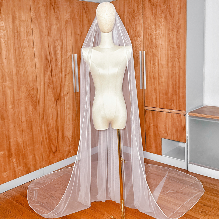 Cathedral length single tier ribbon edge wedding veil cascading down a display torso.