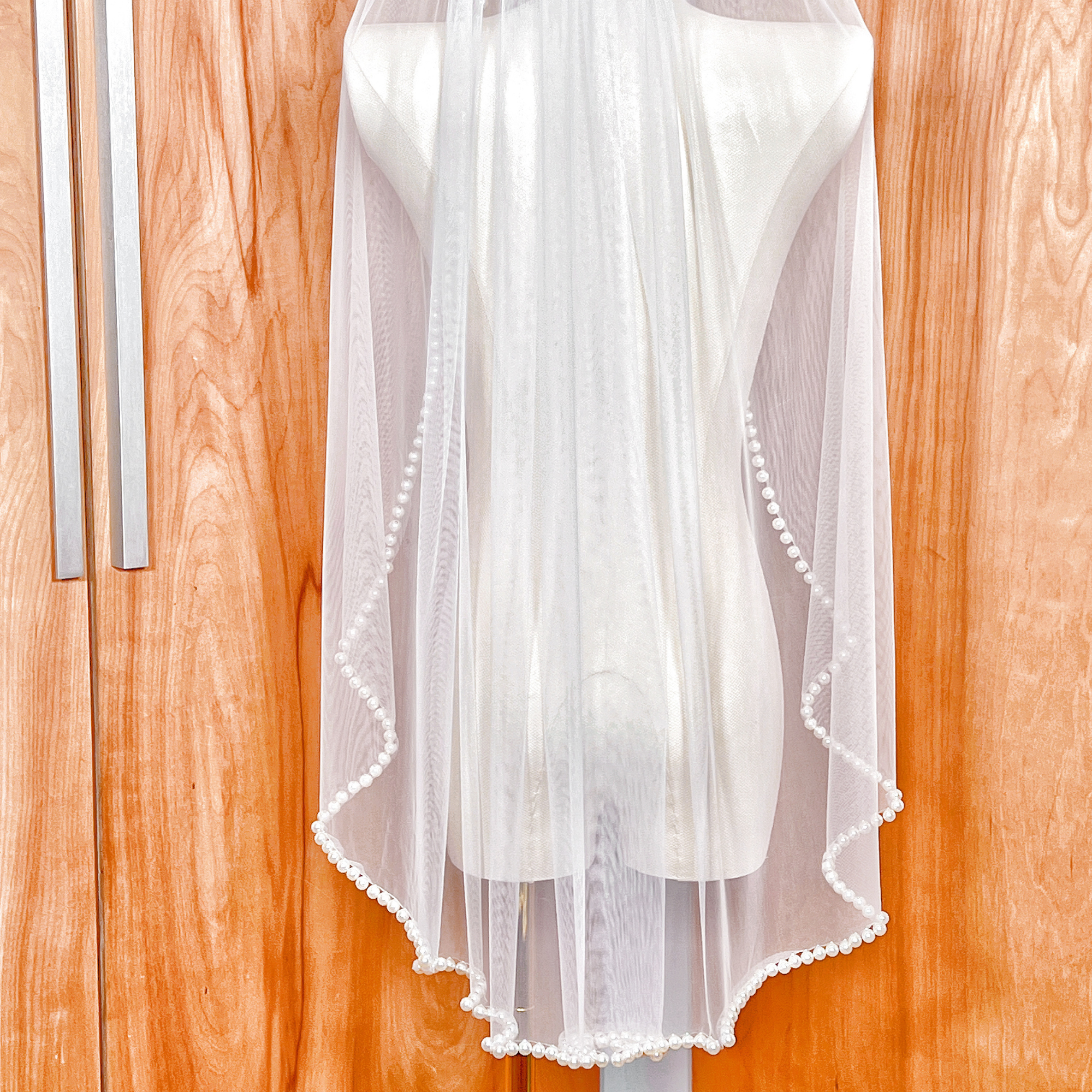 Soft ivory wedding veil in a hip-length cut with a continuous row of lustrous pearls along the hem.