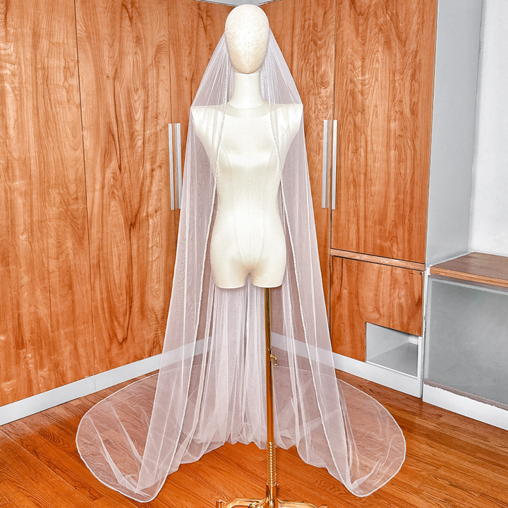 Cathedral length soft tulle wedding veil with a delicate beaded edge displayed on a bridal mannequin.