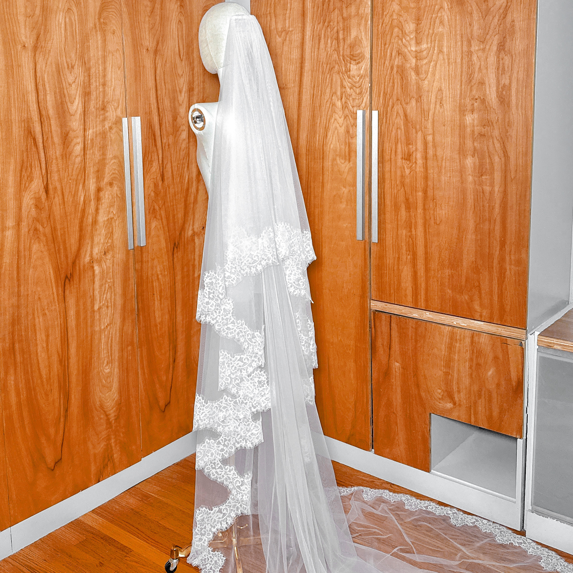 Soft tulle two tier Chantilly lace trim veil in cathedral length draped for a bridal look.