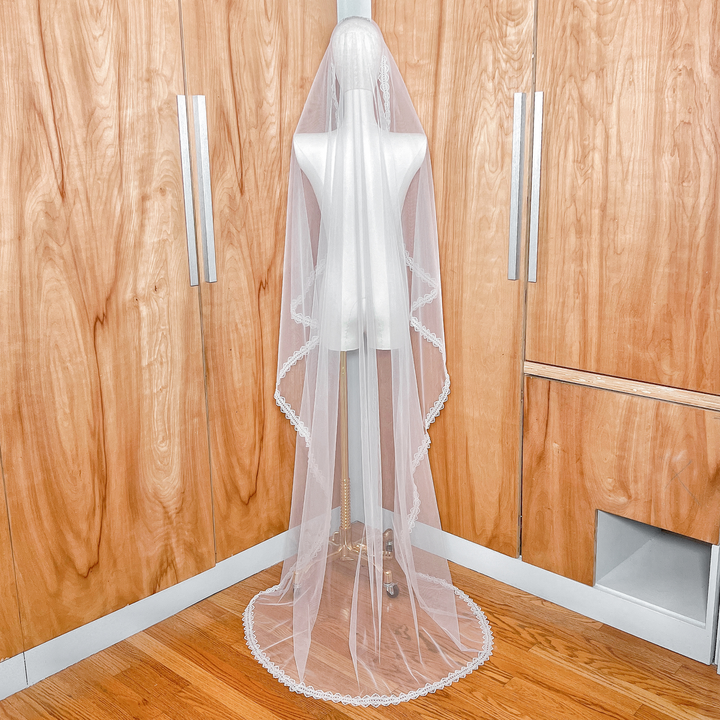 Back view of a floor-length bridal mantilla veil on a mannequin, highlighting the elegant drape and detailed lace finish.