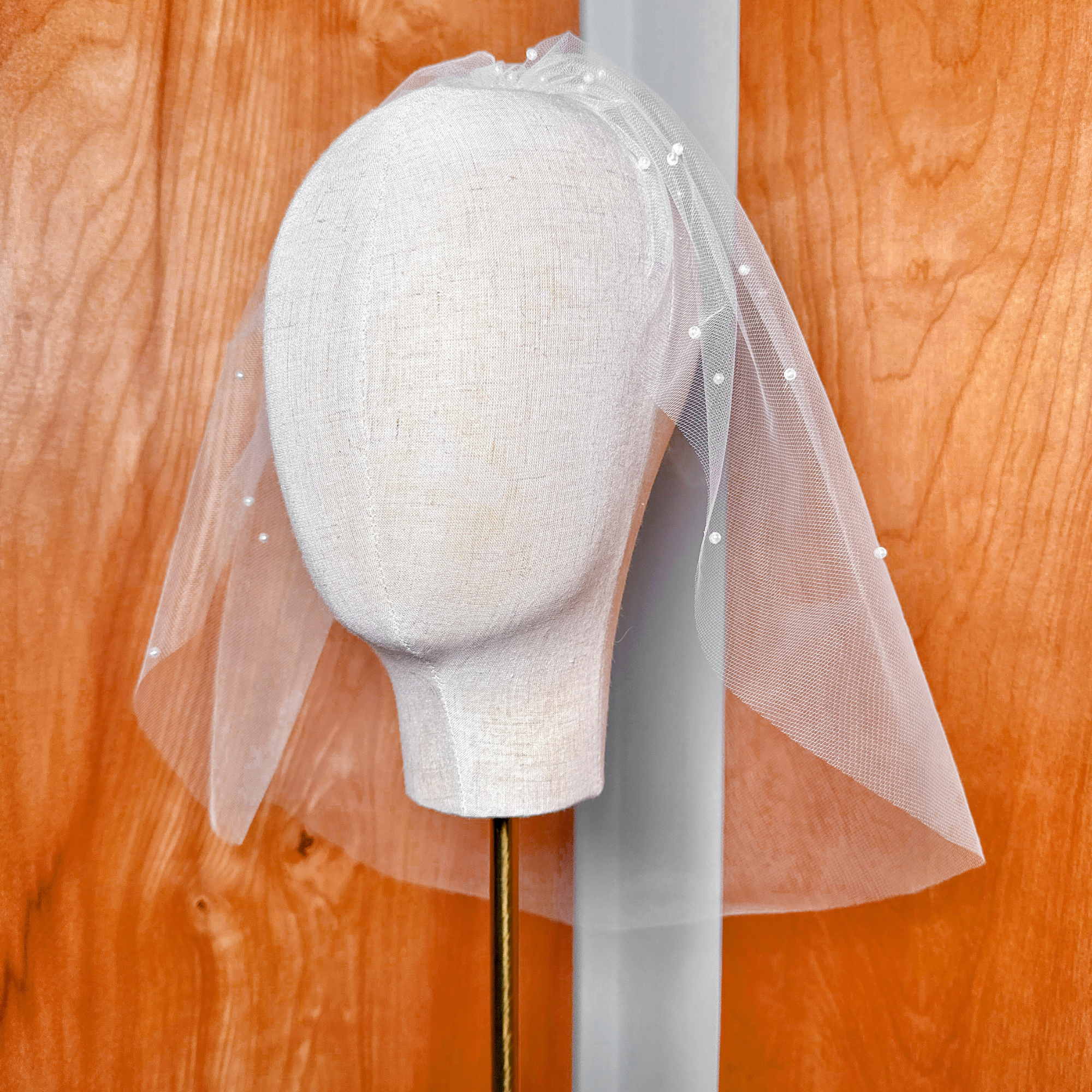 Full studio presentation of a classic ivory pearl birdcage wedding veil on a display headform.