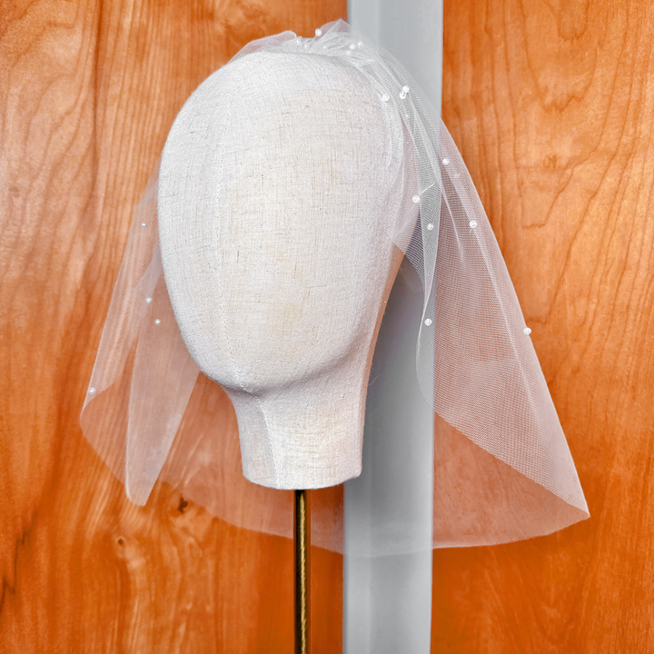 Full studio presentation of a classic ivory pearl birdcage wedding veil on a display headform.