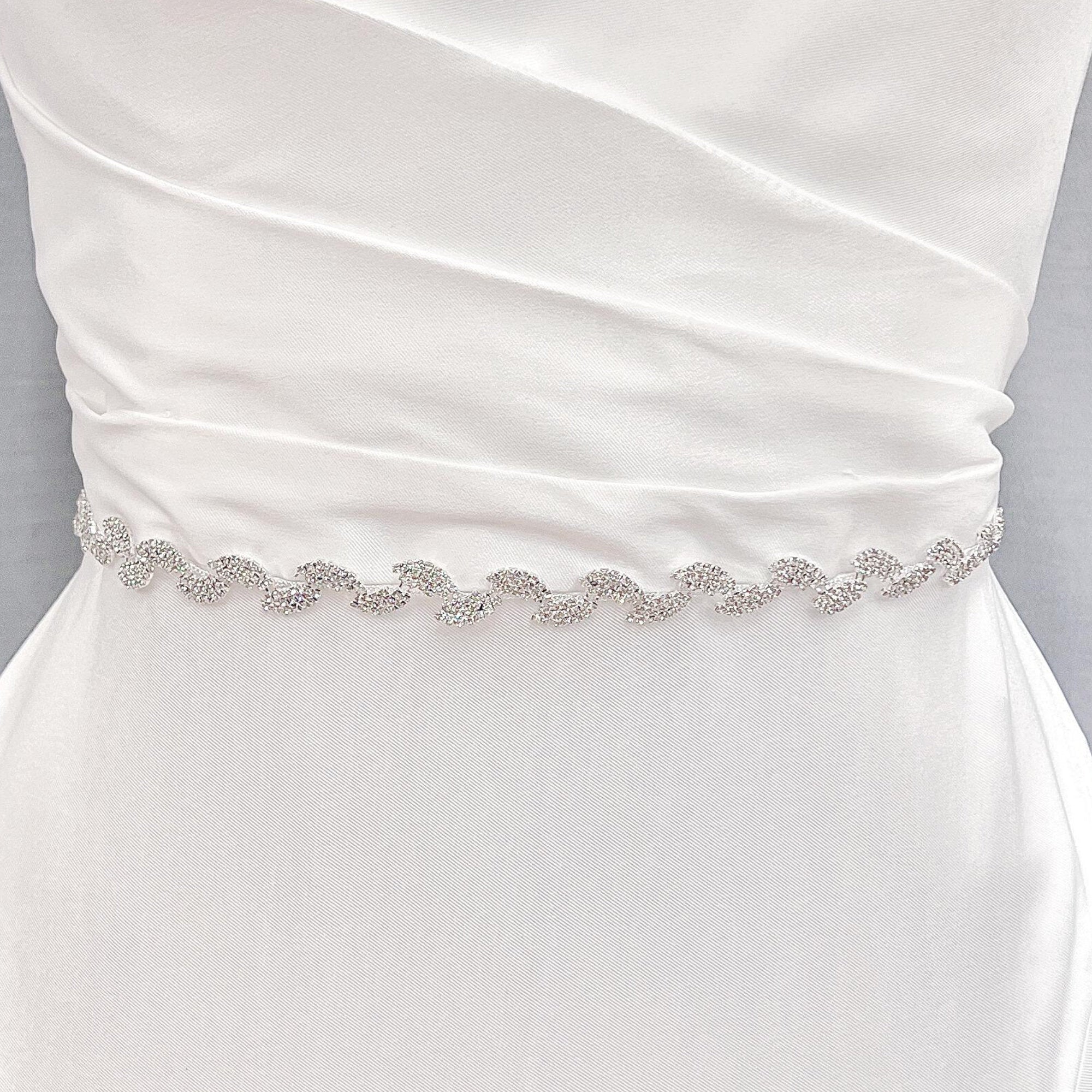 Thin silver crystal bridal belt sparkling against a white satin wedding gown fabric background.