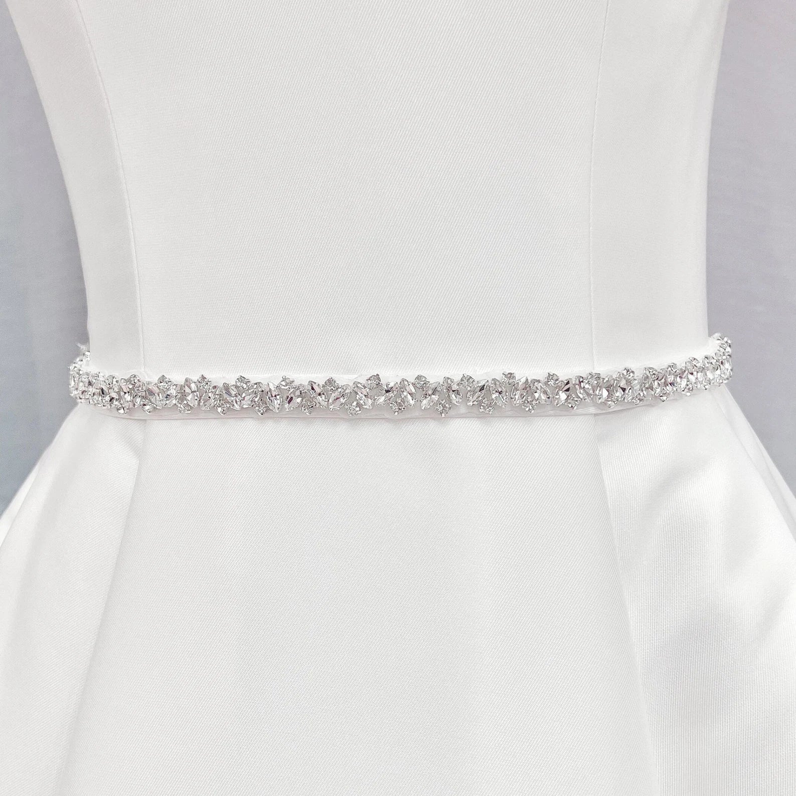 Front view of a thin silver rhinestone bridal belt tied around the waist of a wedding dress form.