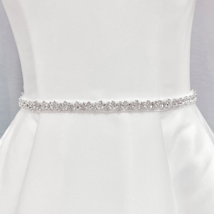 Front view of a thin silver rhinestone bridal belt tied around the waist of a wedding dress form.