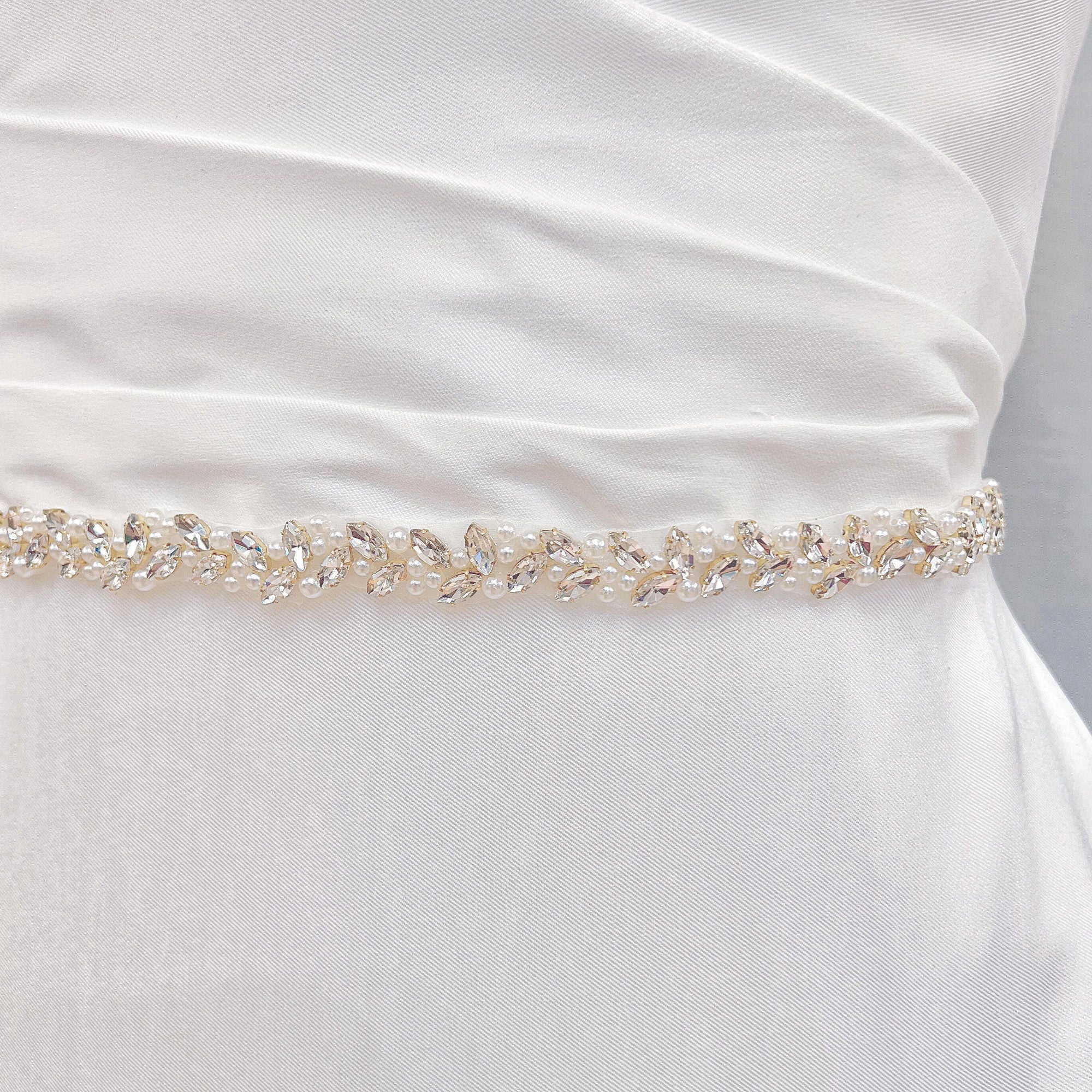 A classic thin simple pearl bridal belt accenting a white bridal gown fabric draped over a mannequin.