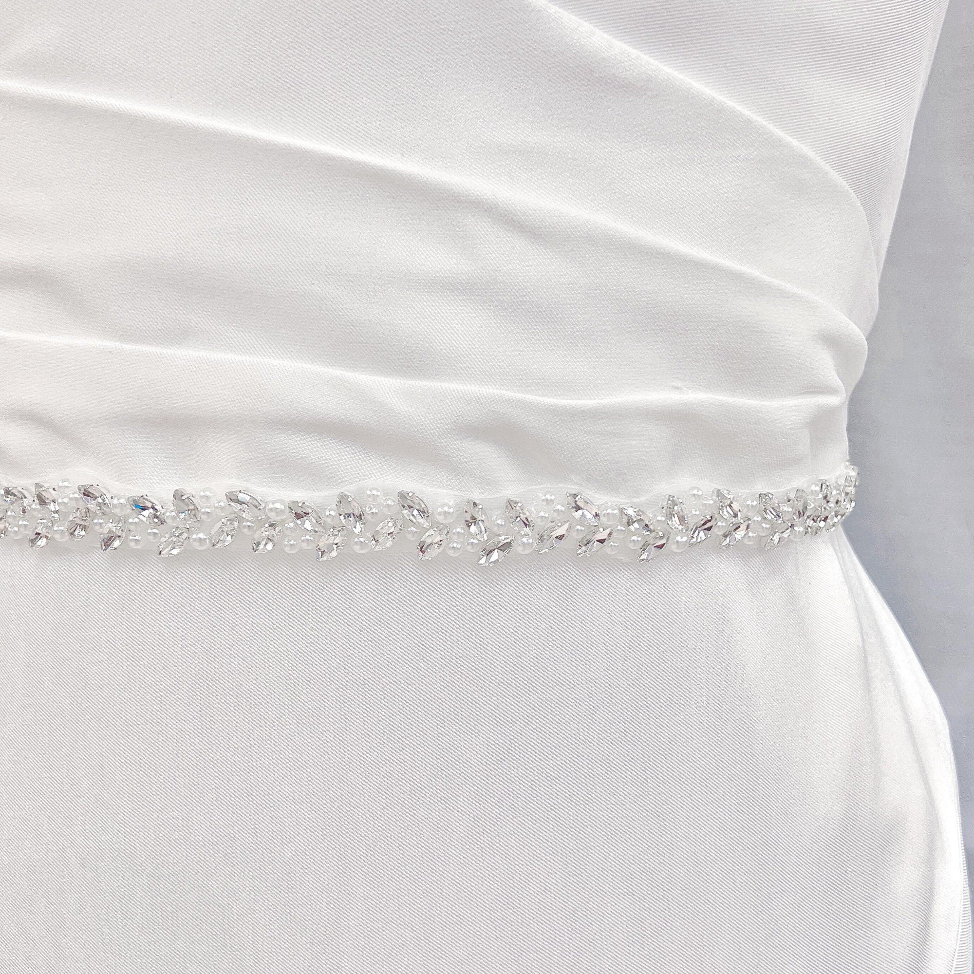 Close-up view of the intricate beadwork on a thin simple pearl bridal belt shown on a mannequin.