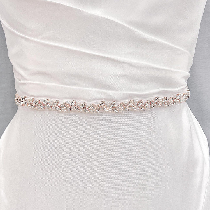 A thin simple pearl bridal belt styled around the waist of a wedding dress on a display mannequin.