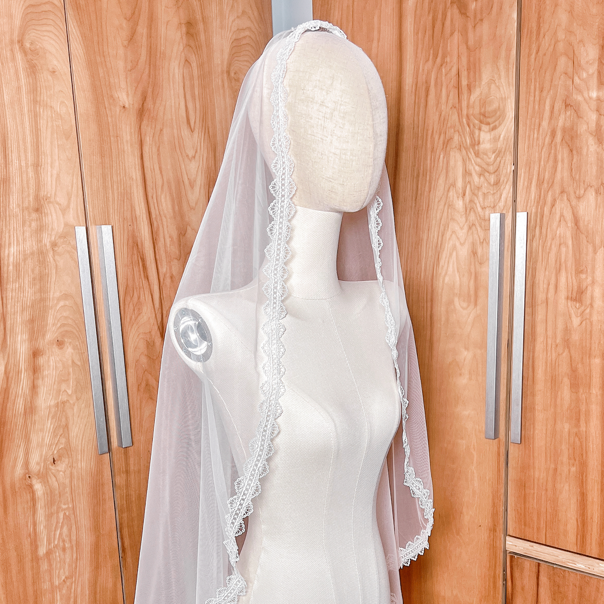 Ivory floor-length bridal mantilla veil featuring a scalloped lace border draped flat over a mannequin's head to frame the face.