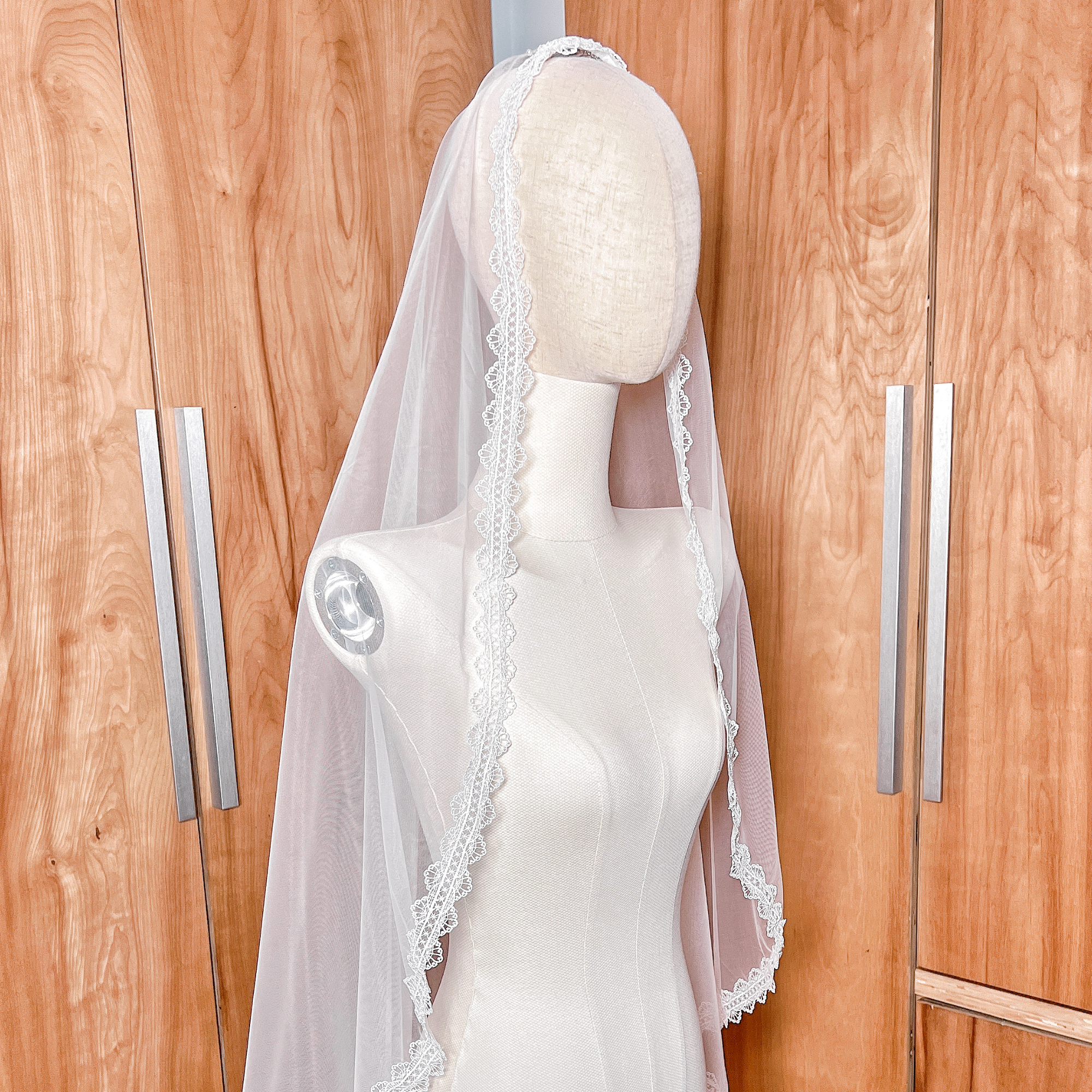 Ivory floor-length bridal mantilla veil featuring a scalloped lace border draped flat over a mannequin's head to frame the face.