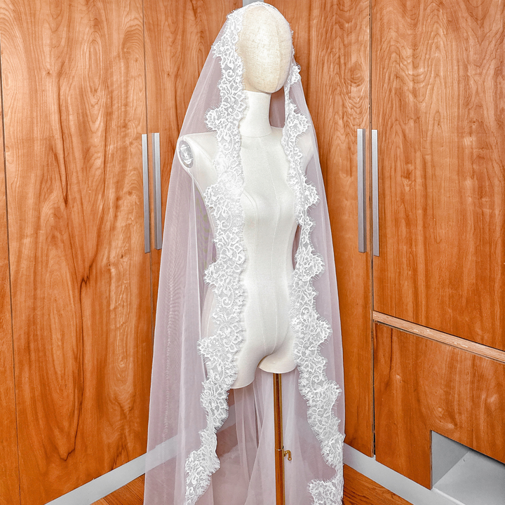 Traditional Spanish-style mantilla wedding veil made of Chantilly lace, displayed in cathedral length on a dress form.