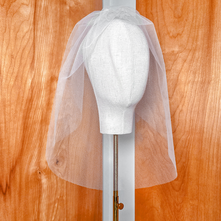Tulle birdcage wedding veil displayed on a bridal bust showcasing the delicate ivory netting and face-framing length.