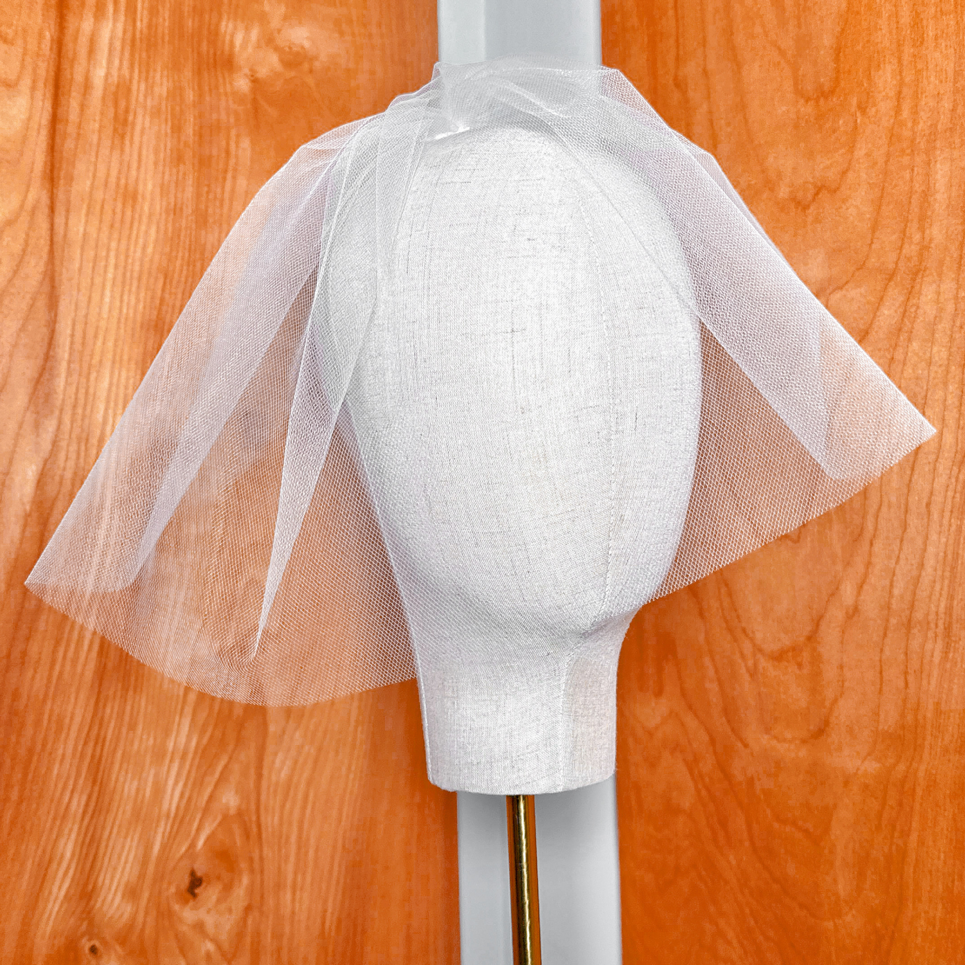 Front view of a white tulle birdcage wedding veil layered neatly on a display bust.