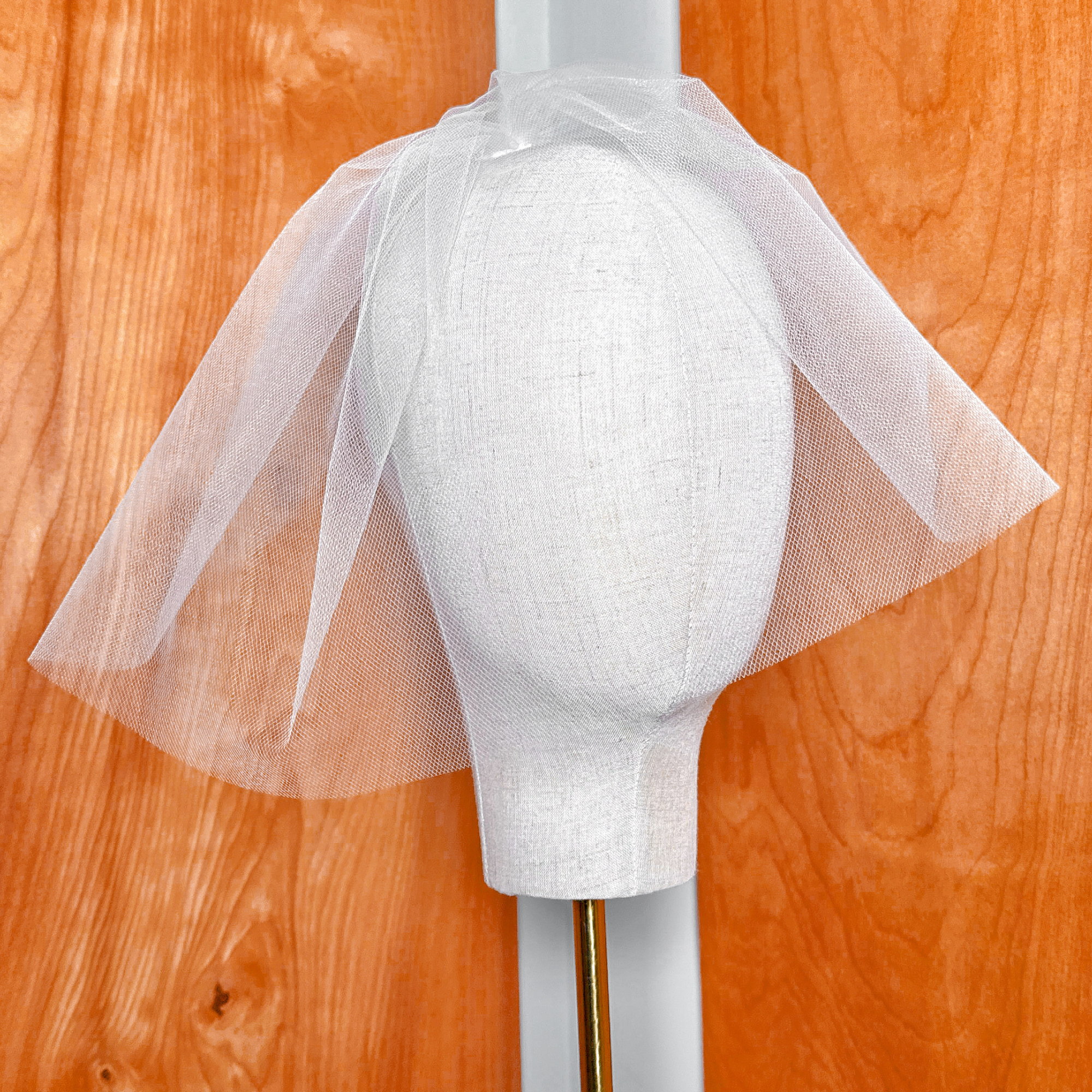 Front view of a white tulle birdcage wedding veil layered neatly on a display bust.