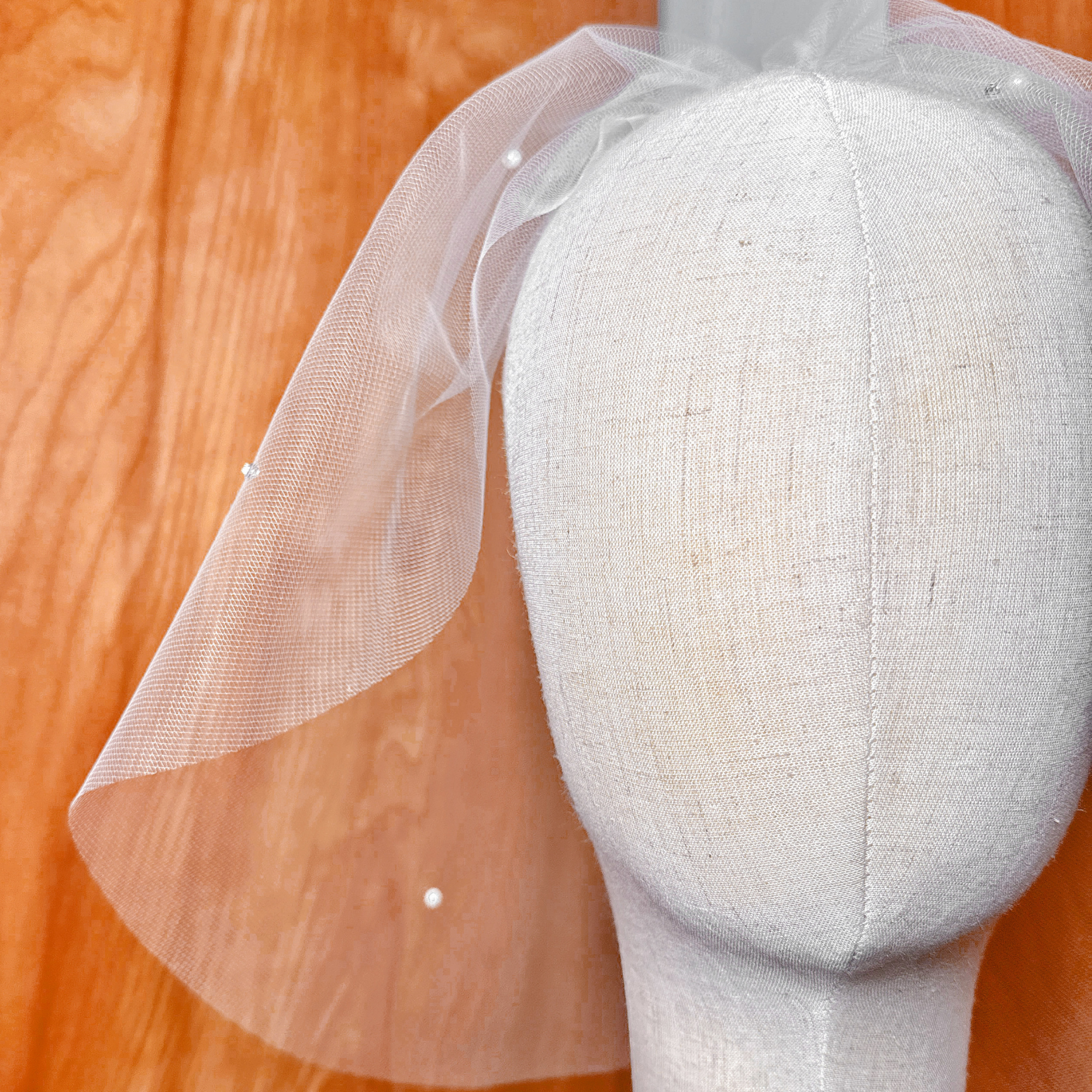Detailed close-up of rhinestones and pearls hand-stitched onto a tulle birdcage wedding veil.