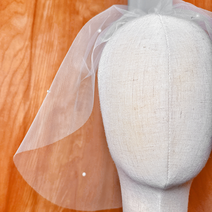 Detailed close-up of rhinestones and pearls hand-stitched onto a tulle birdcage wedding veil.