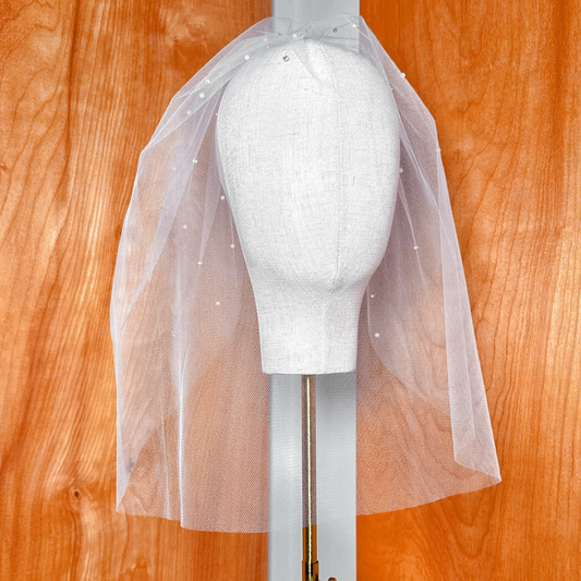Front view of a tulle birdcage wedding veil with rhinestones and pearls on a display bust.