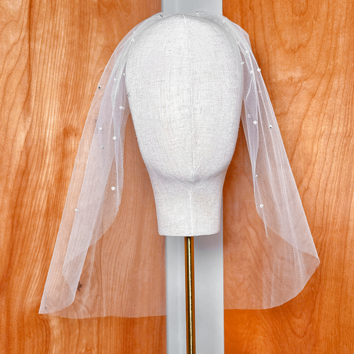 Top-down angle showing the placement of rhinestones and pearls across the tulle birdcage wedding veil.