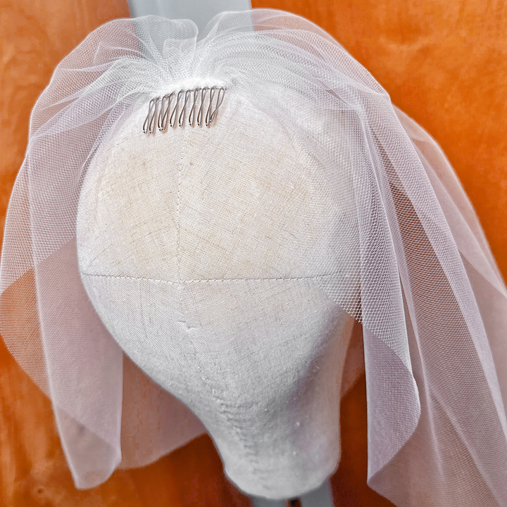 Side profile view of a tulle birdcage wedding veil demonstrating its structure, volume, and secure comb attachment.