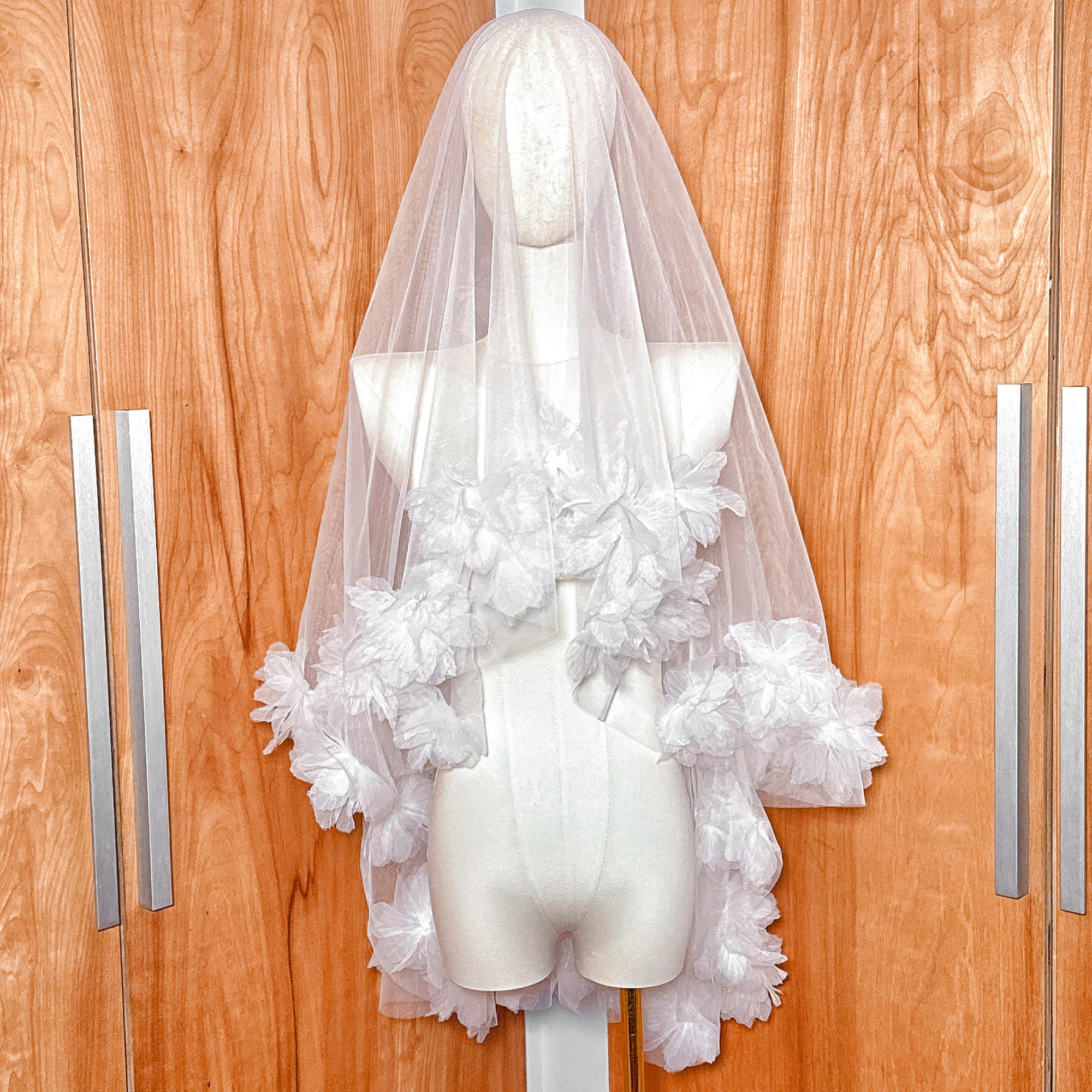 Front view of a two tier 3D flower wedding veil in fingertip length displayed on a bridal mannequin.