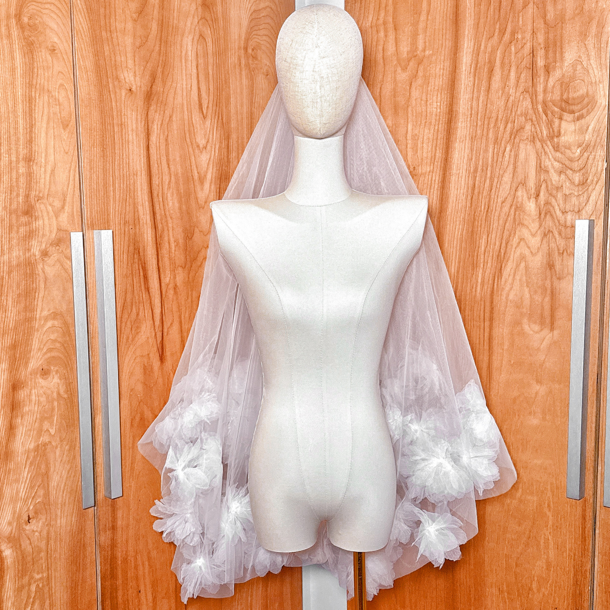 Lightweight fingertip length two tier 3D flower wedding veil draped over a bridal mannequin.