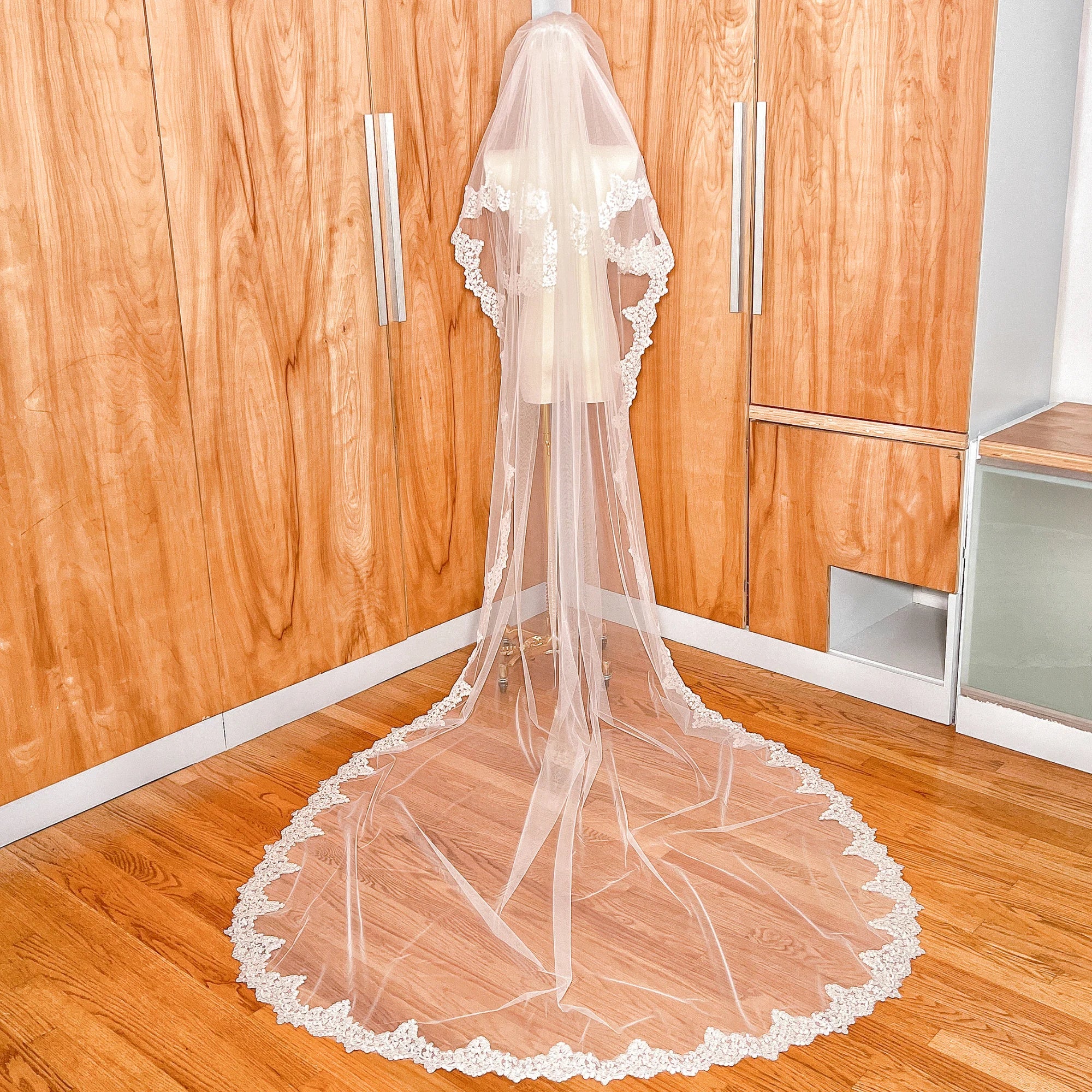 A cathedral length Two Tier Alençon Lace Wedding Veil with Blusher showcasing its flowing silhouette on a display mannequin.