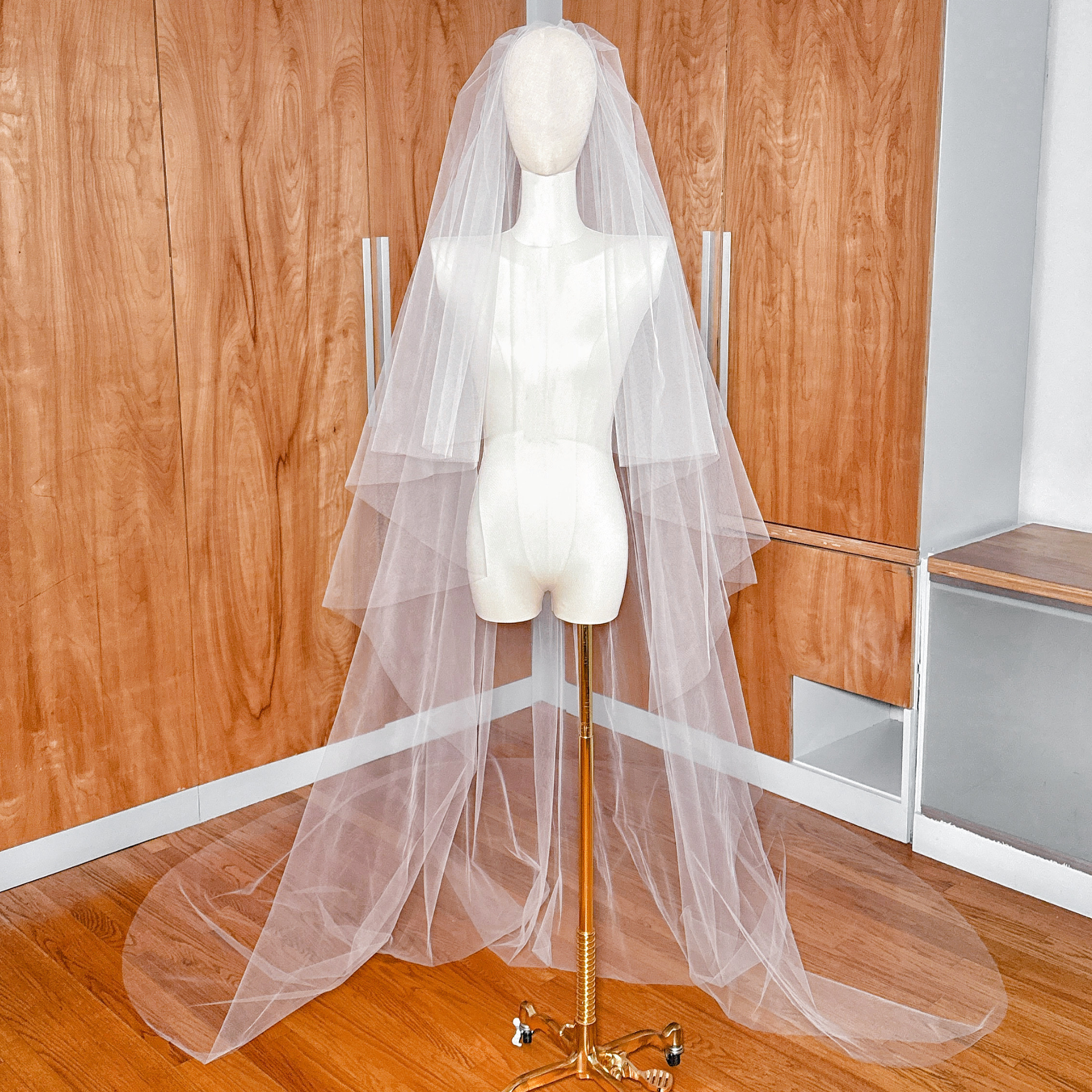 A two-tier cathedral tulle wedding veil with a raw edge and blusher draped over a mannequin.