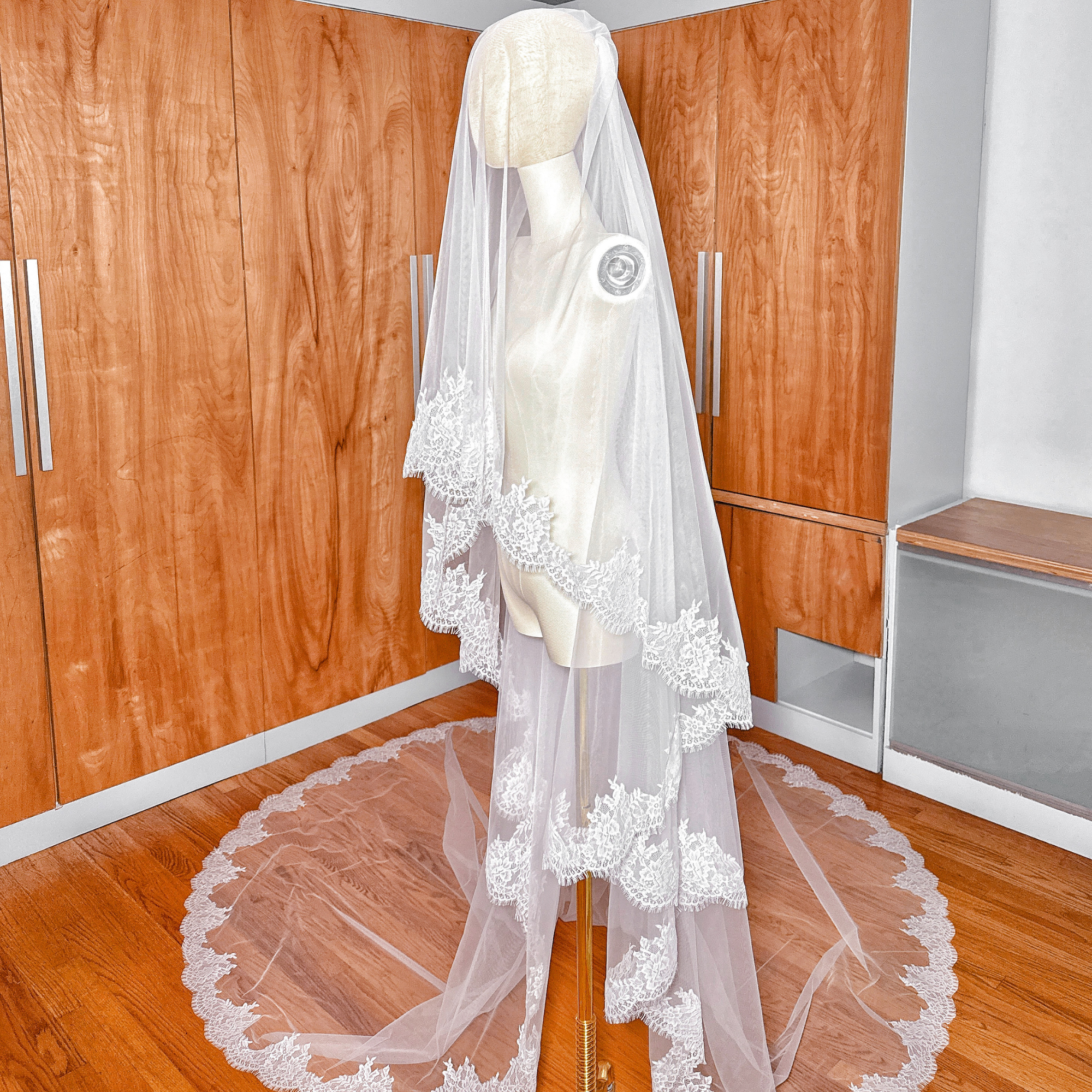 Side profile of a cathedral length two tier Chantilly lace veil on a mannequin, demonstrating the volume and tiered layering of the tulle.