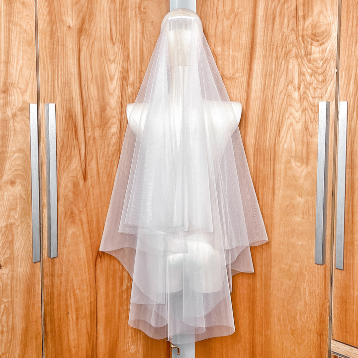 Close-up of the metal hair comb attachment on a two-tier fingertip length wedding veil with raw edges.
