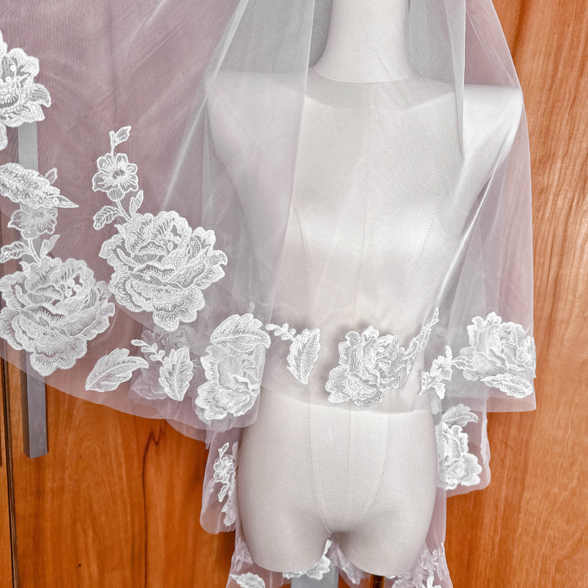High-angle shot of a two tier floral lace wedding veil in fingertip length on a display mannequin.