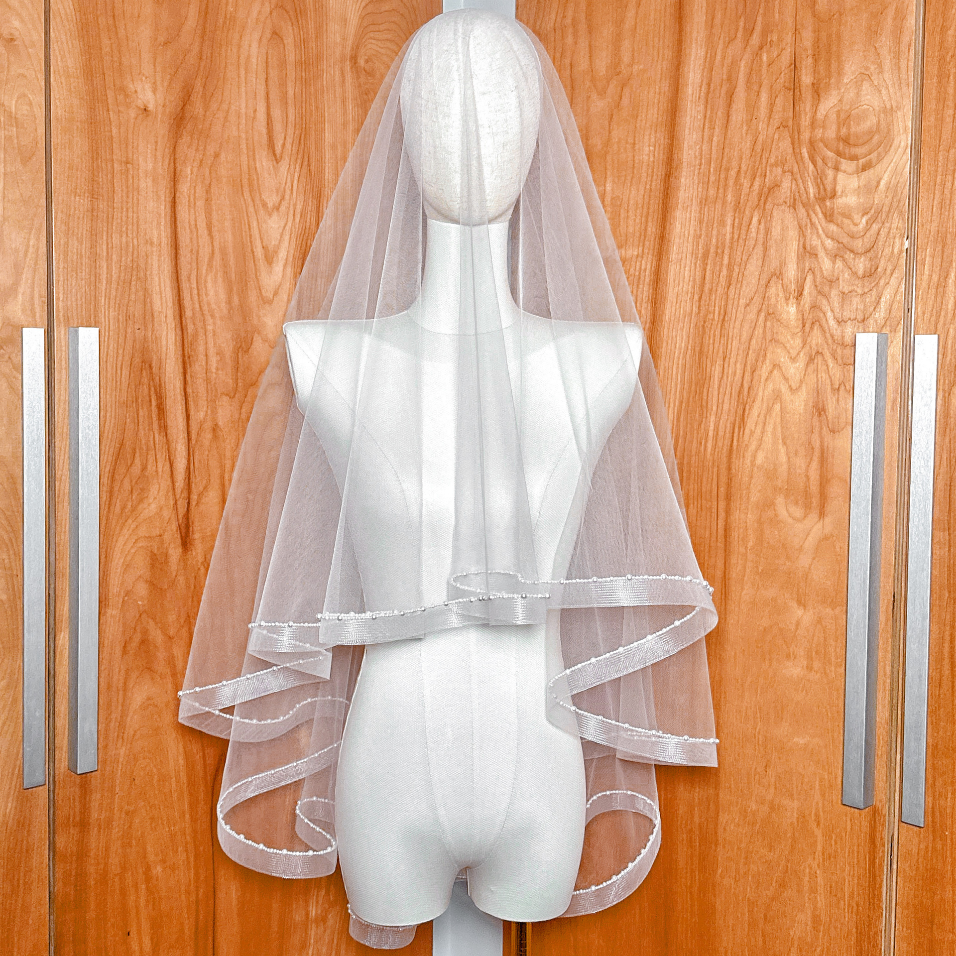 A two-tier fingertip length horsehair veil with elegant pearl trim displayed on a mannequin.