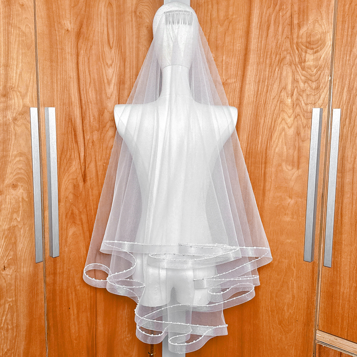 Soft white two-tier horsehair veil featuring a shimmering pearl-trimmed edge, fingertip style.