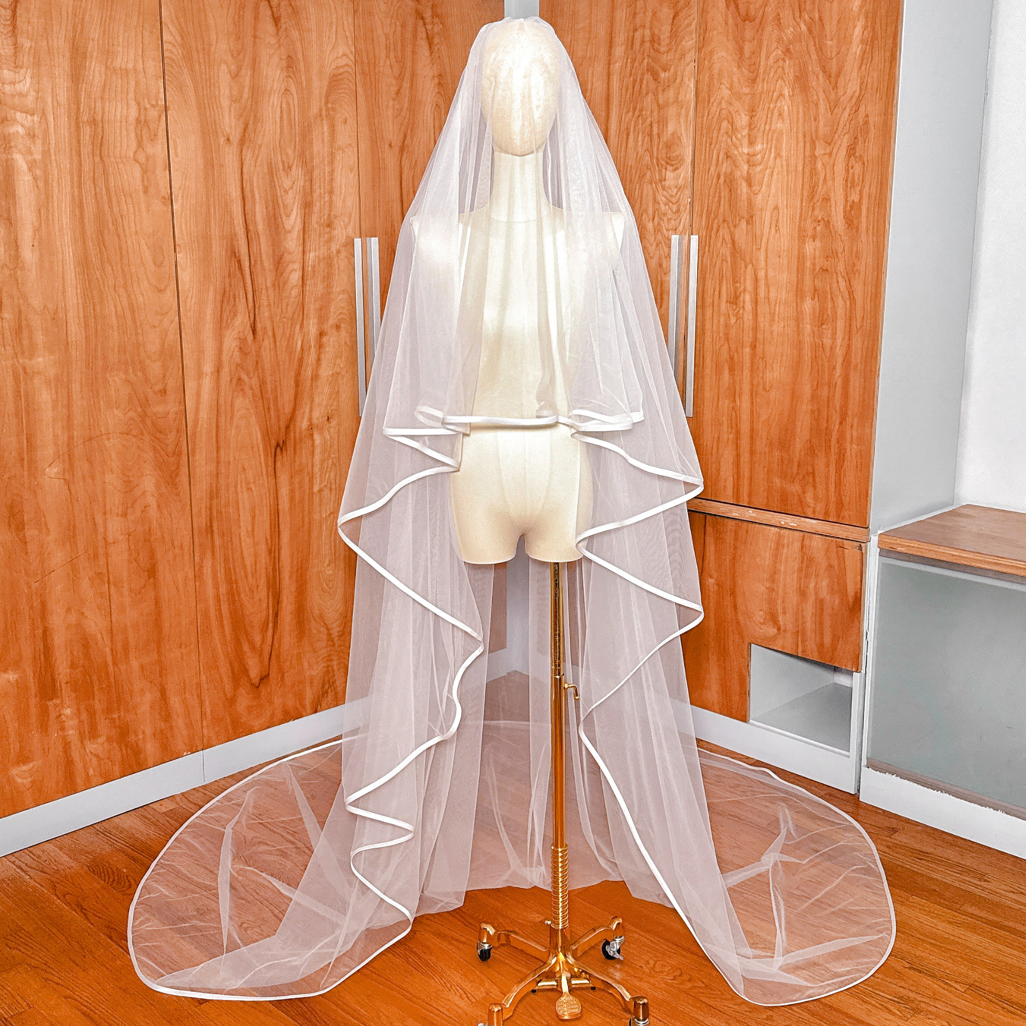 Front view of a cathedral length two tier ribbon edge wedding veil showing the blusher pulled forward over a mannequin.