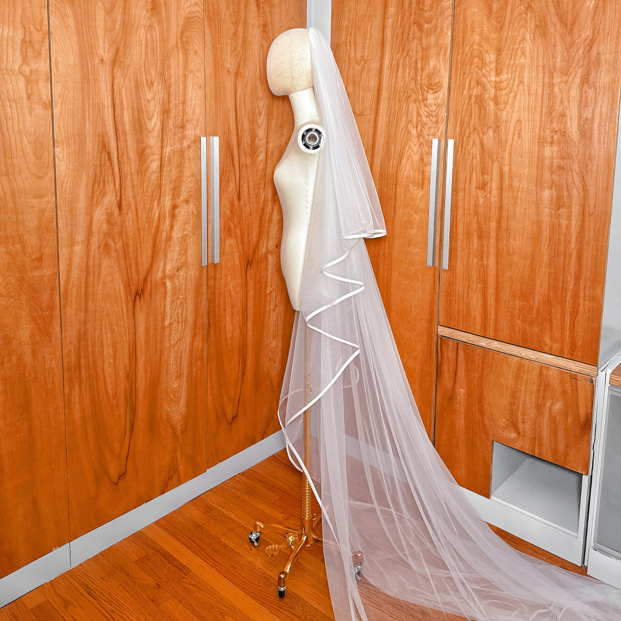 Side profile of a cathedral length two tier wedding veil featuring a crisp ribbon edge design and sheer blusher layer.