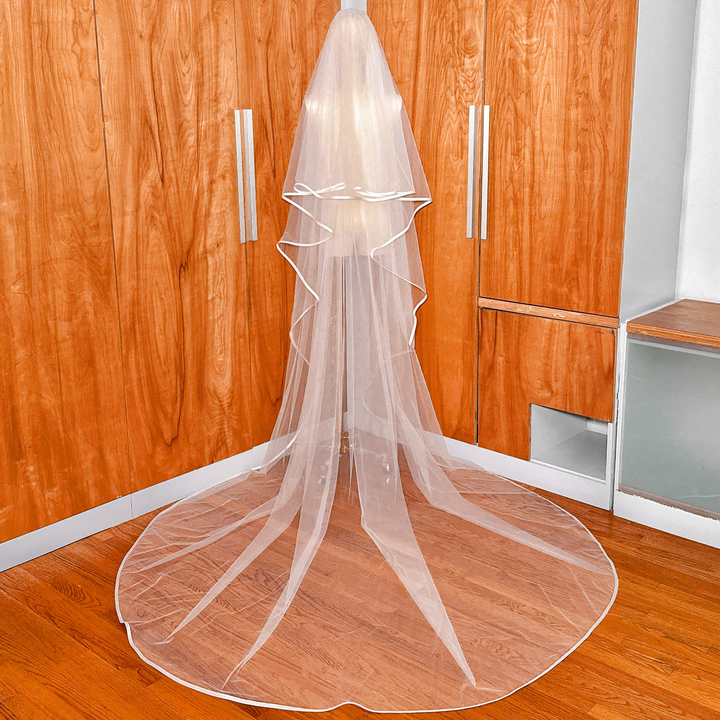 Detailed shot of the sheer bridal tulle, metal comb attachment, and ribbon trim on a two tier cathedral length wedding veil with blusher.