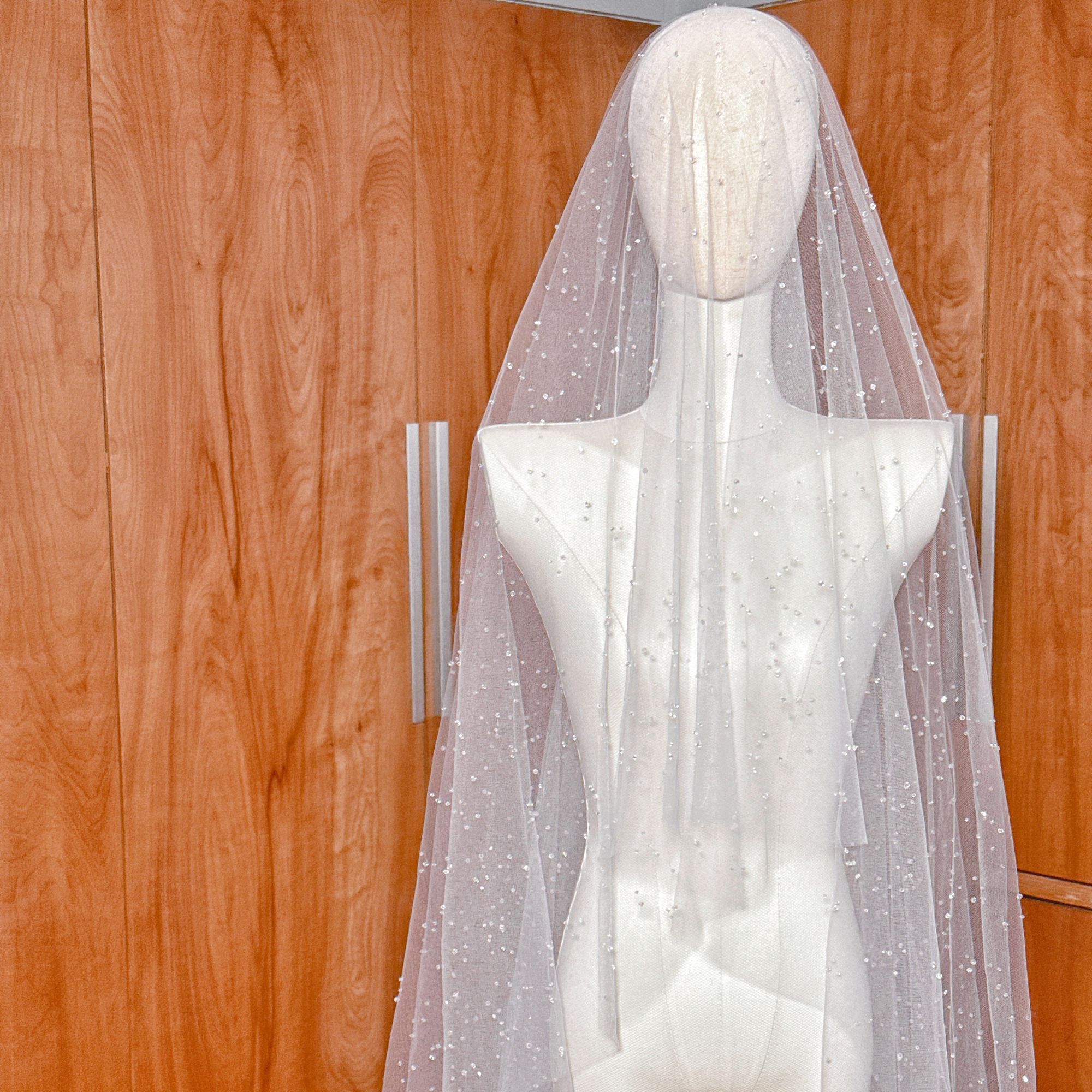 High-quality sheer tulle on a two-tier scattered crystal beaded cathedral veil draped on a mannequin stand.