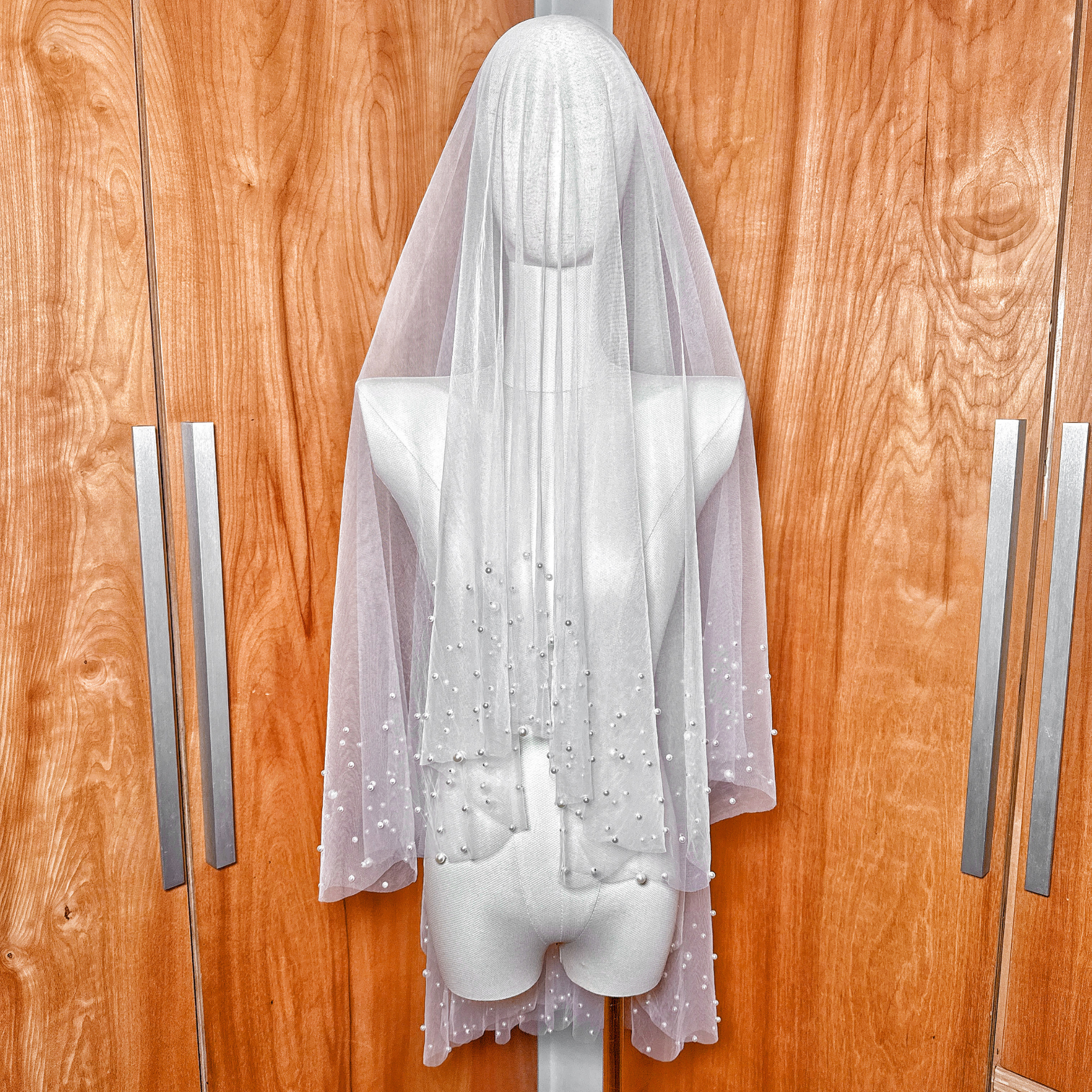 A fingertip length two tier scattered pearl wedding veil in soft tulle draped elegantly.