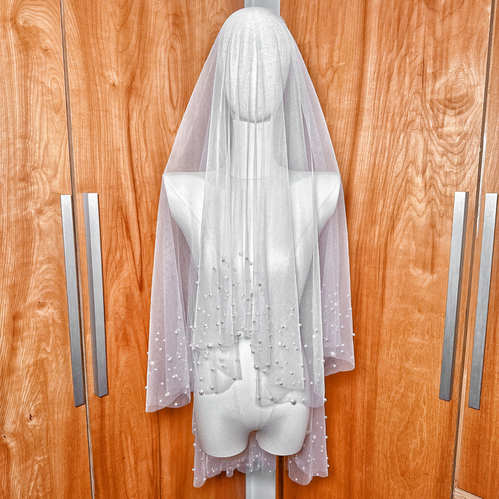 A fingertip length two tier scattered pearl wedding veil in soft tulle draped elegantly.
