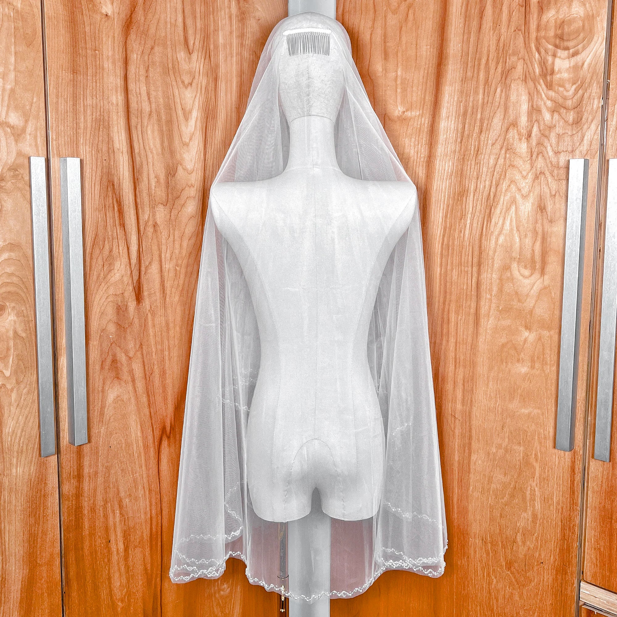 A two-tier wedding veil with a beaded edge in fingertip length, shown on a mannequin.
