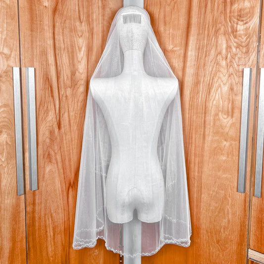 A two-tier wedding veil with a beaded edge in fingertip length, shown on a mannequin.